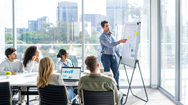 Business people watching a presentation on the whiteboard. A man is writing on the whiteboard with charts and graphs.